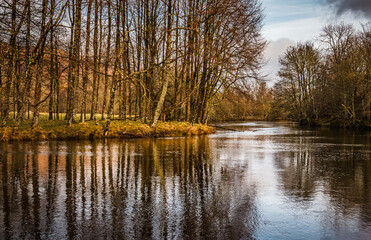 Trees reflecting in the still surface of River Lochay in Killin, on a winter afternoon, with a few boats moored at the local jetty. Perthshite Scotland.