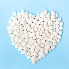 Many white pills are scattered in the shape of a heart on a sky blue background.A new generation antiviral drug.Pandemic, virus, health. Antidepressants, cardio. Sold in a pharmacy with a prescription