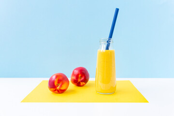 Bright yellow turmeric smoothie in a glass jar with a straw for cocktail, ripe nectarines on a yellow, sky blue background.Healthy nutrition, vegetarianism, detox.A breakfast drink.Refusal of plastic.