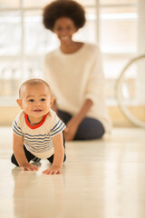 Mother watching baby boy crawl on floor