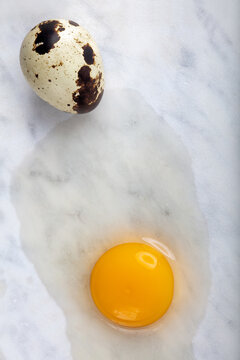Whole fresh quail egg alongside a cracked-open egg with bright yellow yolk