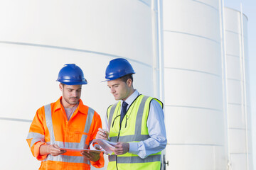 Workers reviewing paperwork next to silage storage towers