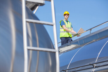 Worker using laptop on platform above stainless steel milk tanker
