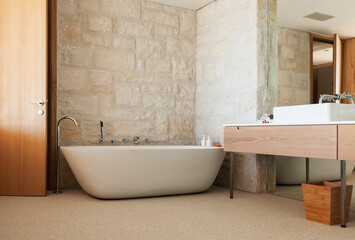 Stone wall behind soaking tub in modern bathroom