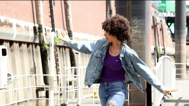 Eine junge dunkelh&auml;utige Frau tanzt auf einer Stra&szlig;e.