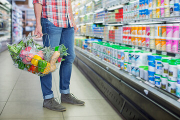 Man carrying full shopping basket in grocery store - obrazy, fototapety, plakaty
