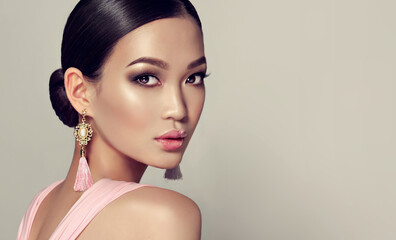 Asian model  fashion girl  with tassel earrings and  pink dress.  Oriental girl model, cosmetics, cosmetology and fashion.
