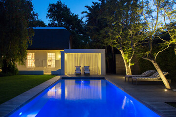 Lawn chairs on wooden deck by illuminated swimming pool at night