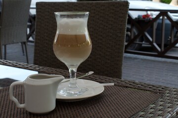 latte coffee with ice in a glass cup on a table in an outdoor cafe on a hot summer day