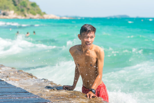 Young Thai man at pier, with water dripping from the body, and sea spray in air, beside wavy turquoise sea in Ko Samet island, Thailand. Sunny day while vacation at tropical beach of Southeast Asia
