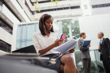 Businesswoman sitting on bench using cell phone outside