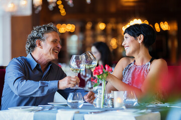 Smiling mature couple raising toast white wine at restaurant table