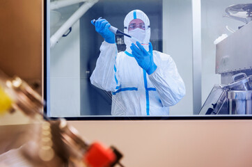 Scientist in clean suit pipetting sample into petri dish in laboratory