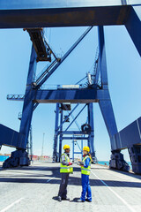 Worker and businessman talking under cargo crane at waterfront