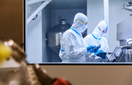 Scientists In Clean Suits Using Digital Tablets In Laboratory