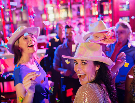 Confetti falling on women wearing cowboy hats laughing dancing in nightclub