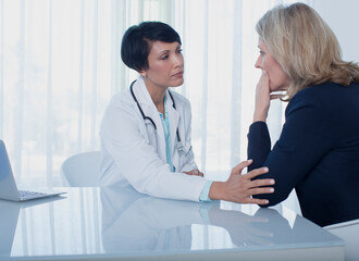 Female doctor consoling sad woman at desk in office