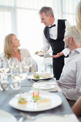 Waiter serving fancy dish to woman sitting at restaurant table
