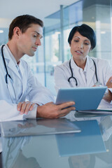 Doctors discussing patient's treatment at desk, using digital tablet