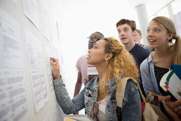 Group of students looking at information board holding books at school