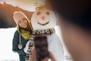 Man photographing woman with snowman