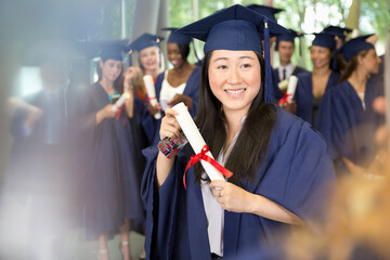 Portrait of smiling female student in graduation gown holding diploma