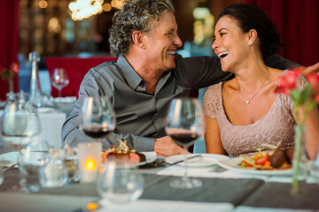 Happy mature couple sitting at restaurant table, wine glasses in foreground