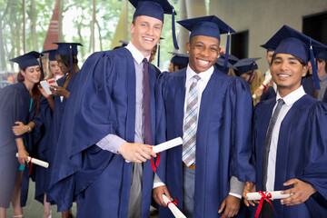 Portrait three smiling male students in graduation gowns holding diplomas