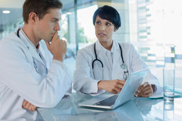 Female and male doctor using laptop in hospital office