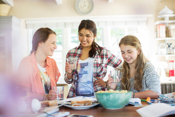 Three teenage girls drinking and eating at table in kitchen