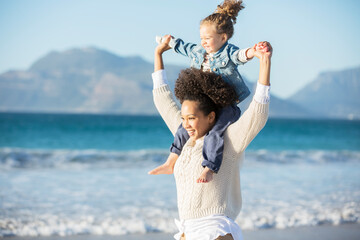 Mother carrying daughter on her shoulders on beach