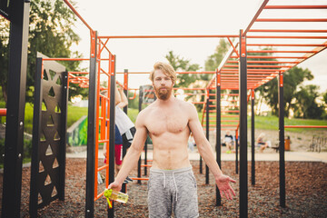 Obraz premium Sporty muscular man drinking water in gym. Thirsty and dehydration from workout and losing too much sweats. Exhausted male athlete drinking water after sports training. Fitness guy taking break