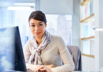 Female office worker sitting at desk using computer, portrait