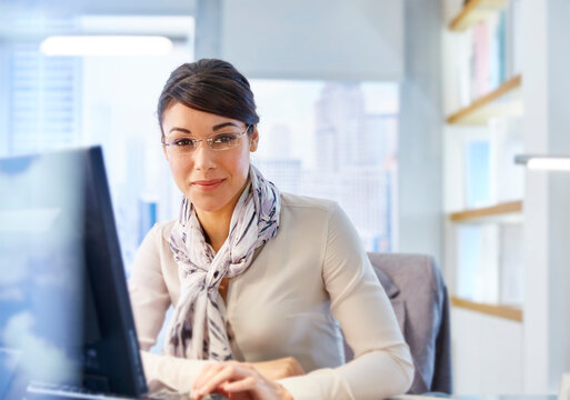 Female office worker sitting at desk using computer, portrait