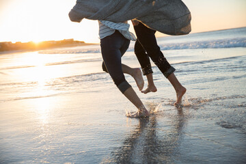 Legs of young couple running on beach at sunset