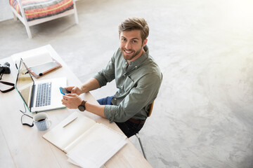 Portrait of young man sitting at desk with mobile phone and laptop