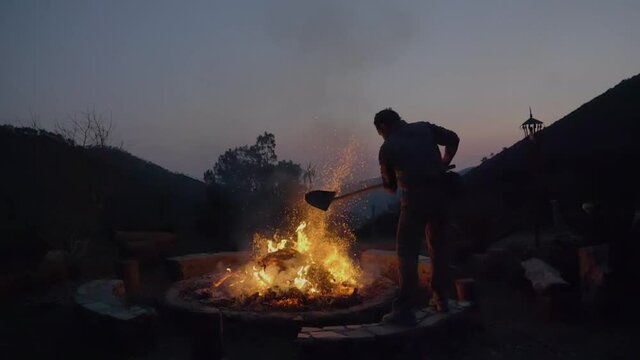 Silhouette of a man stoking the fire of the bonfire. Man burning furniture in nature, fire and ashes. 4k