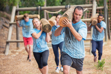 Determined people running with logs on boot camp obstacle course - obrazy, fototapety, plakaty