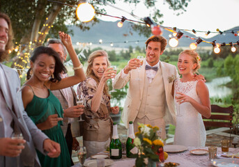 Young couple guests toasting champagne during wedding reception in domestic garden