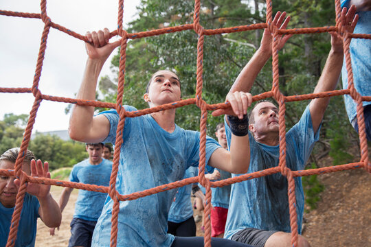 Determined woman climbing net at boot camp obstacle course