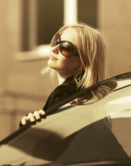 Happy young fashion woman in sunglasses leaning on her car