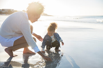 Mother and daughter drawing on wet sand on beach