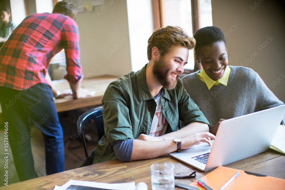 Wall mural Smiling casual business people working at laptop in office