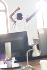 Casual businesswoman wearing headphones dancing in office
