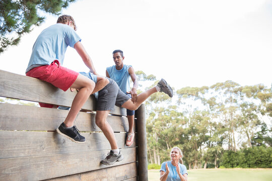 Teammates helping man over wall on boot camp obstacle course