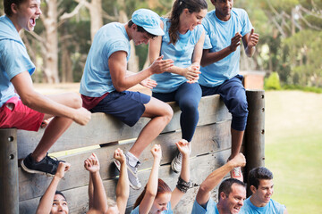 Cheering team at wall on boot camp obstacle course