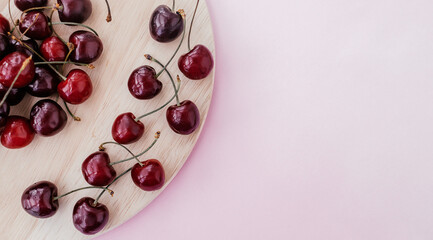 Sweet cherry on a wooden cutting board on a pink background.Summer sweet concept. Copy space for text