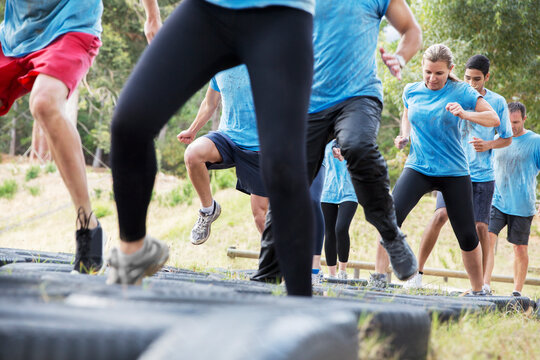 Determined people jumping tires on boot camp obstacle course