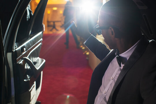 Celebrity in limousine arriving at red carpet event waving to photographing paparazzi
