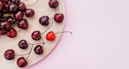 Sweet cherry on a wooden cutting board on a pink background.One bright red heart-shaped berry.Summer sweet concept. Copy space for text